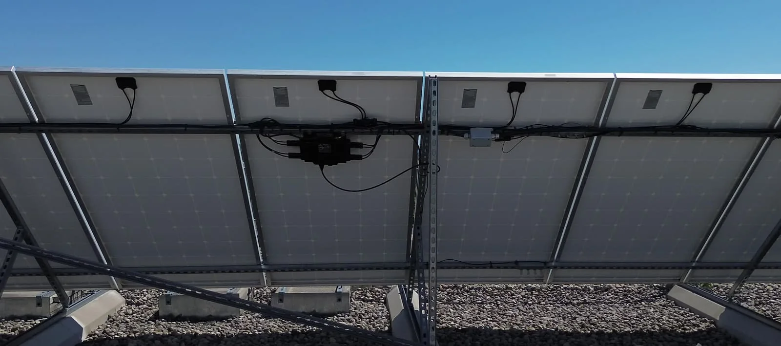 The back of a ground-mounted array on a gravel roof, one Quad hung on the rail between its panels